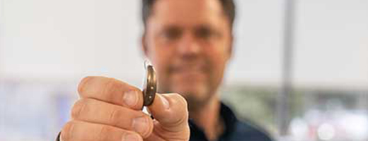 Image of Justin Osmond showing a standard hearing aid in his hand